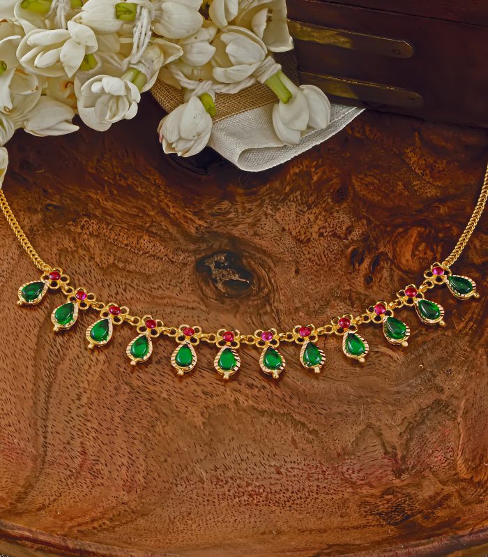 Traditional gold Nagapadam necklace with green teardrop pendants and red stone floral connectors.