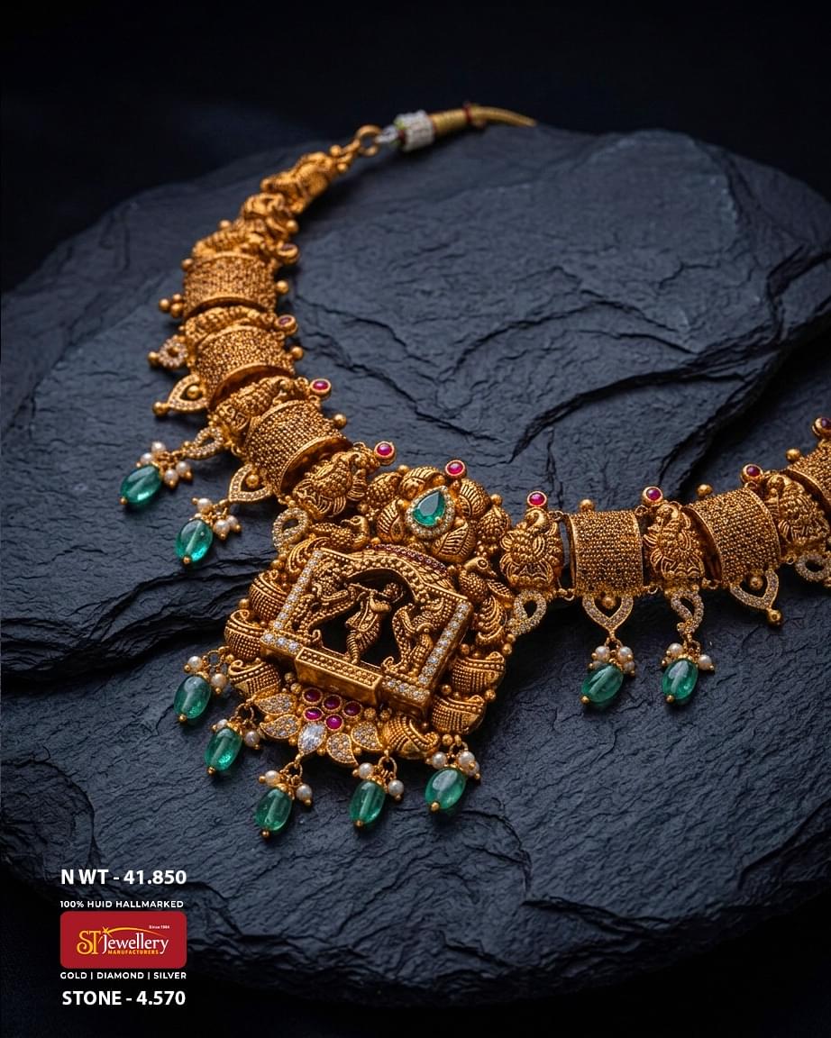 Antique temple gold bridal necklace featuring a divine temple deity centerpiece, intricate handcrafted motifs, emerald green gemstone drops, pearl accents, and traditional South Indian heritage craftsmanship.