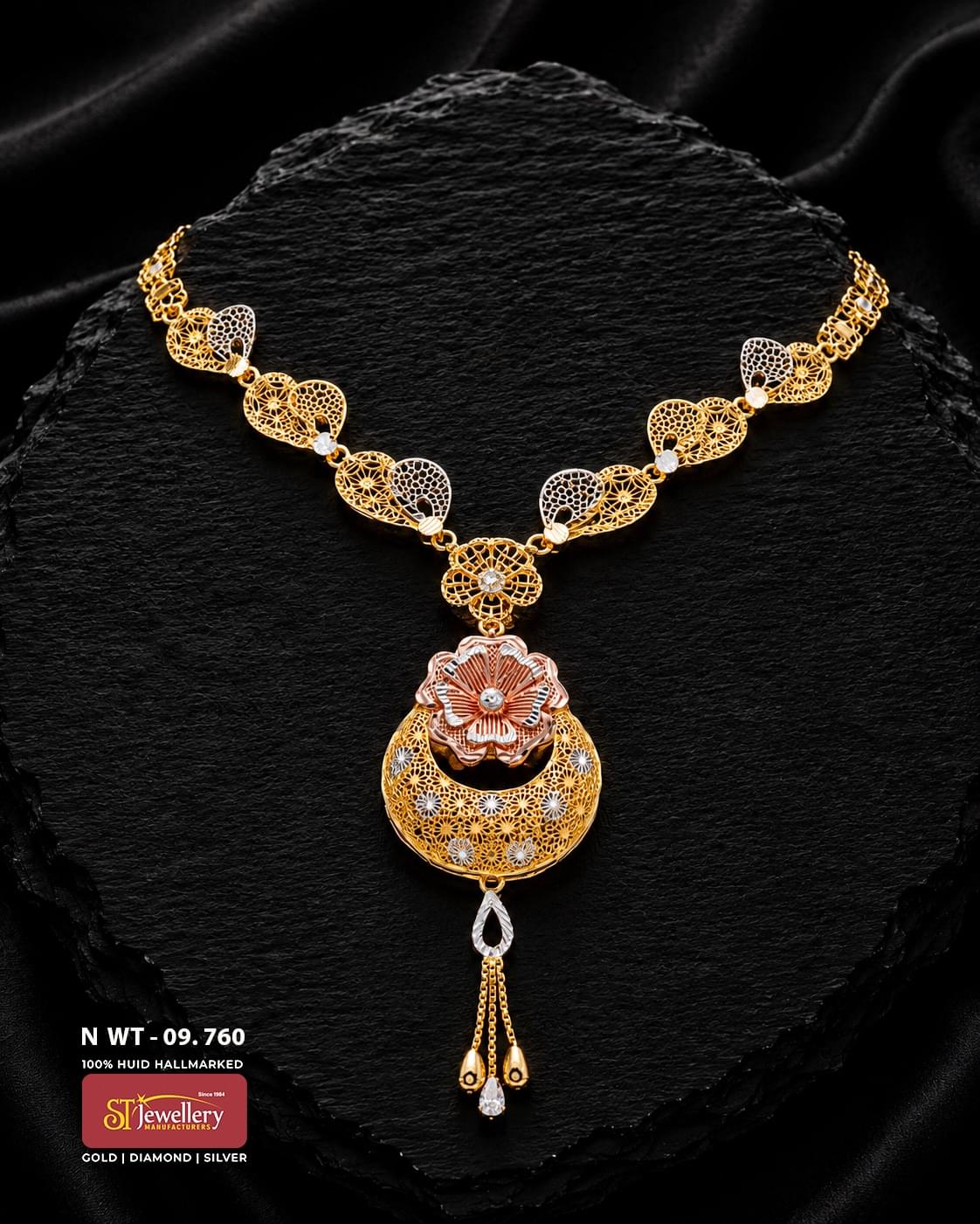 Gold necklace with intricate filigree leaf motifs, white and rose-gold accents, a layered floral pendant and delicate teardrop hanging elements displayed on a black textured background.