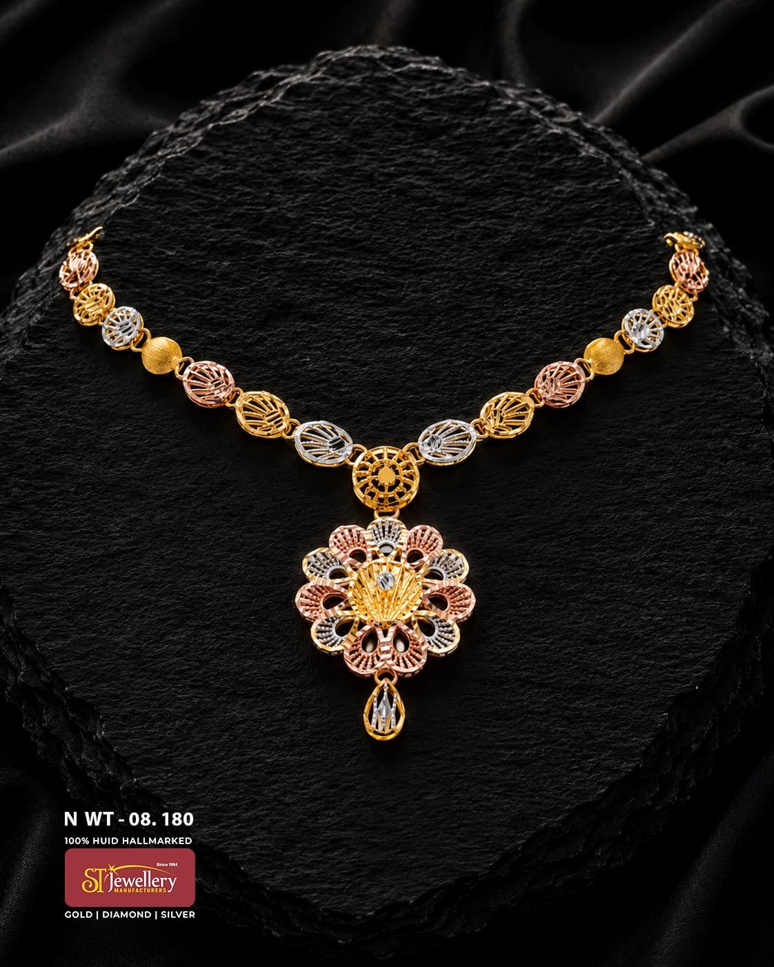 Multitone gold necklace with decorative oval links in yellow, rose and white-gold tones, featuring an intricate flower-shaped pendant and a single teardrop hanging detail on a black textured background.