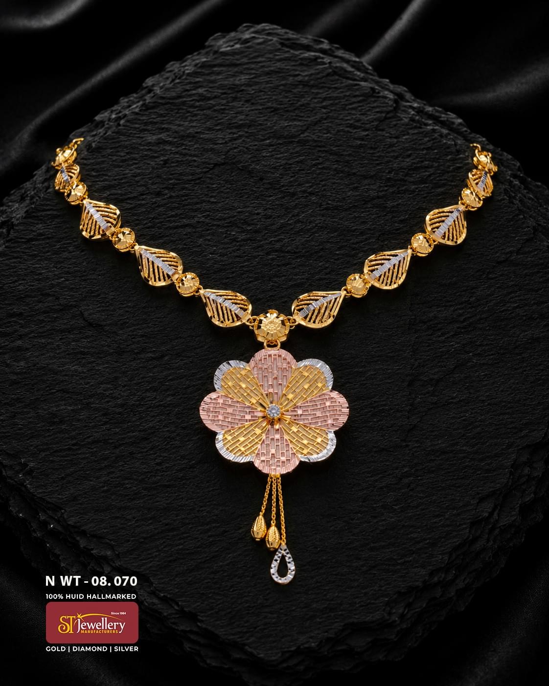Multitone gold necklace with leaf-shaped links, a large layered floral pendant in yellow, rose and white-gold tones, and three delicate hanging drops displayed on a black textured background.