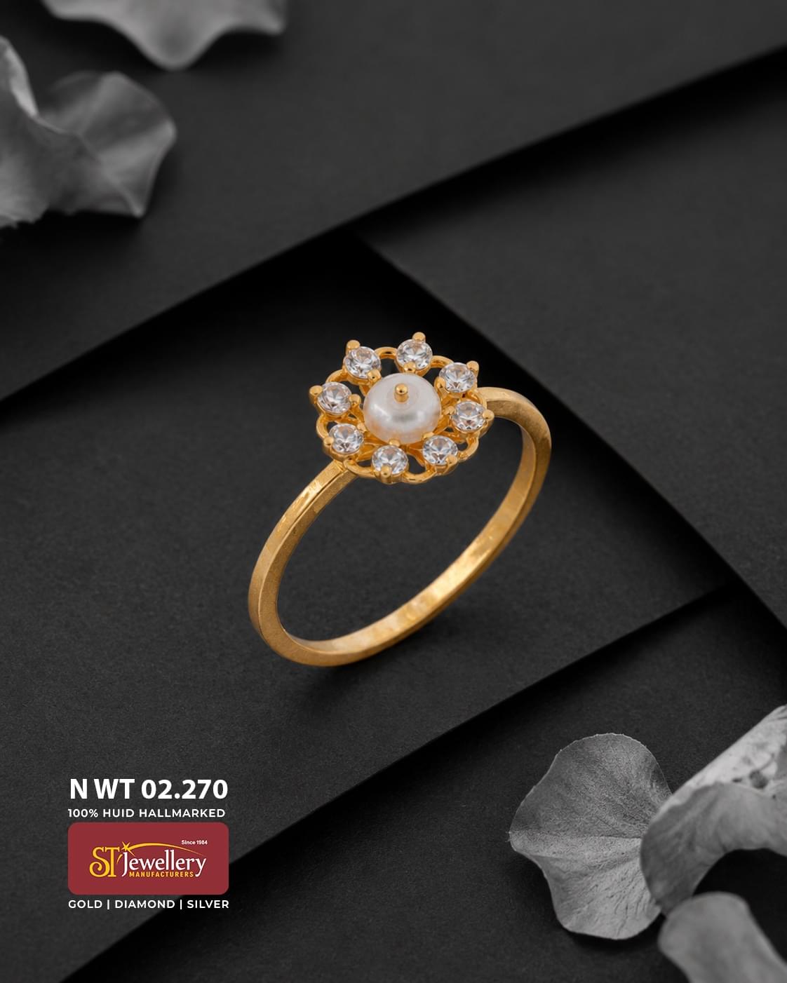 Elegant gold ring featuring a floral design with a central white pearl surrounded by sparkling clear stones, displayed on a matte black background.