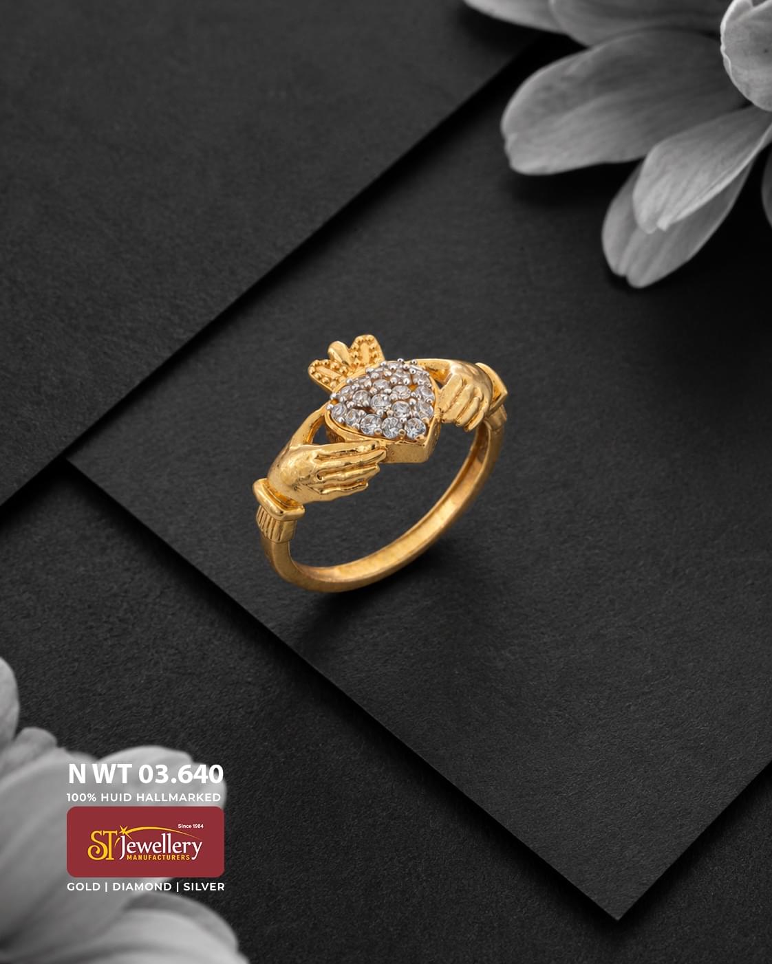 Elegant gold ring featuring a heart-shaped centre filled with sparkling clear stones, framed by detailed hand and crown motifs, displayed on a matte black background.