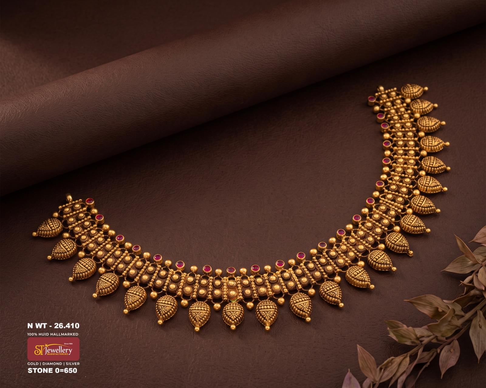 Traditional antique gold necklace with intricate repeating motifs, red stone accents, gold bead detailing, and engraved leaf-shaped dangling elements.